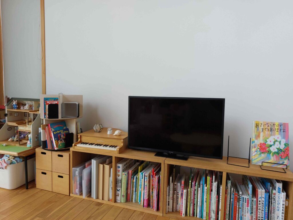 小森羊仔先生のご自宅の絵本コーナーの写真。テレビの台の下にたくさんの本が並べられている。